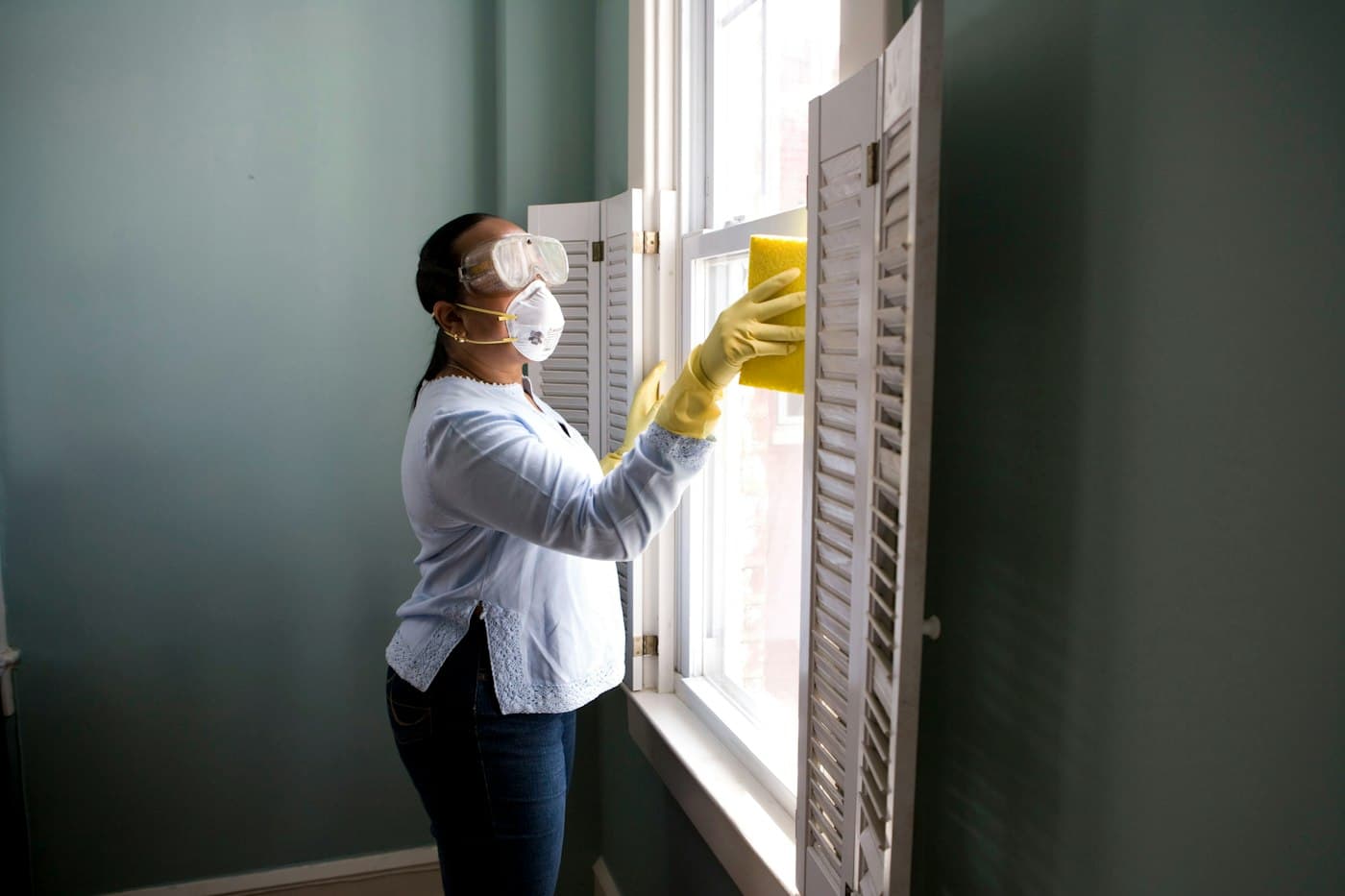 A cleaner wiping down window shutters in a bright room